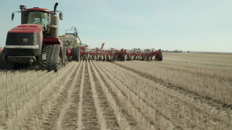 Exhilarating-low-sideways-flight-close-up-view-of-red-farm-seeding-tractor-machine-traveling-on-flat-farmland-rows-of-crop-on-sunny-day,-Vanguard,-Saskatchewan,-Canada,-aerial