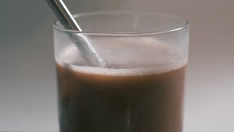 Iced-coffee-drink-in-glass-being-sucked-up-with-stainless-steel-straw---close-up