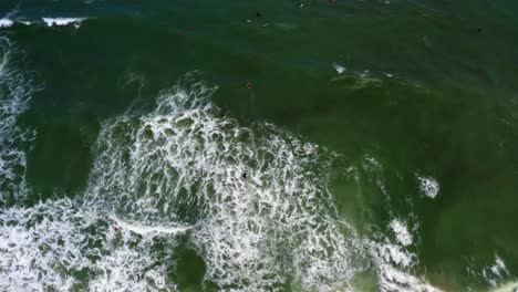 Aerial-top-drone-shot-of-a-surfer-swimming-out-past-waves-at-the-famous-beach-Praia-do-Amor-near-the-tropical-tourist-city-of-Pipa-in-Northern-Brazil-on-a-warm-sunny-summer-day