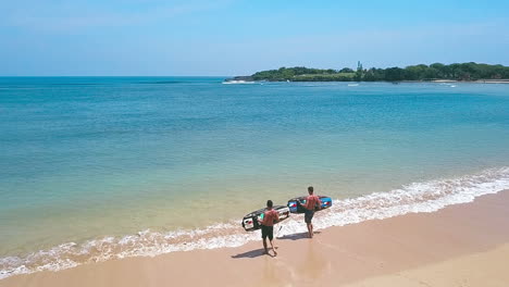 Two-young-men-taking-Jetsurf-boards-out-on-a-beautiful-beach-in-Bali,-slow-motion