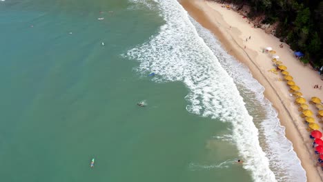 Wunderschöne-Luftdrohne-Vogelperspektive-Vorbeiflug-Des-Tropischen-Strandes-Praia-Do-Madeiro-Mit-Bunten-Sonnenschirmen-Und-Touristen-Und-Surfern-In-Der-Nähe-Der-Berühmten-Stadt-Pipa-Im-Norden-Brasiliens