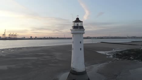 Low-tide-aerial-view-coastal-lighthouse-sunrise-shipping-port-cranes-horizon-rising-tilt-down