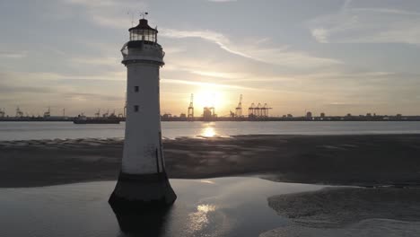 Low-tide-aerial-view-coastal-lighthouse-reveal-sunrise-shipping-port-cranes-horizon-orbit-right-pull-back