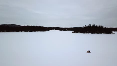 Aerial-shot-of-a-snowmobile-rider-alone-in-the-immensity-of-a-frozen-lake-in-Chibougamau,-Quebec