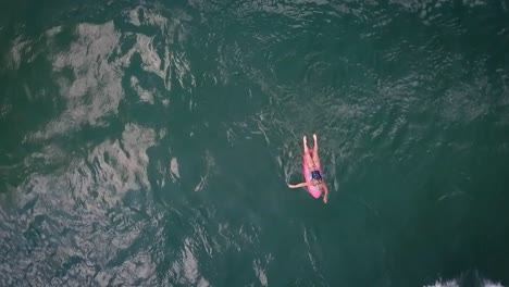 Weiblicher-Wake-Surfer-Blick-Von-Oben,-Der-In-Zeitlupe-Auf-Einem-Rosa-Surfbrett-In-Richtung-Boot-Paddelt