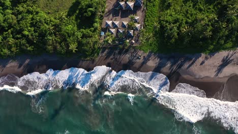 Rising-aerial-shot-of-beach-and-waves-during-sunset-with-small-village-in-south-east-asia