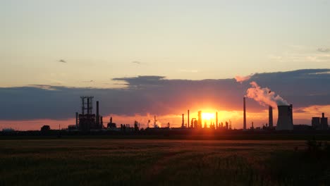 Leuchtend-Rot-oranger-Sonnenuntergang-über-Ölraffinerie,-Weizenfeld-Im-Vordergrund,-4k