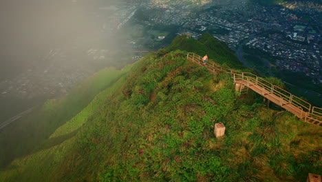 Man-running-at-stairway-to-heaven,-aerial-tracking-shot-at-sunset,-Hawaii