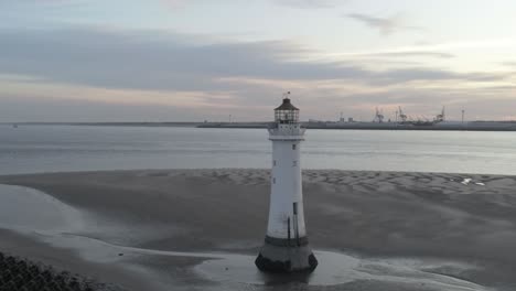 Low-tide-aerial-view-coastal-lighthouse-sunrise-shipping-port-cranes-horizon-wide-left-orbit