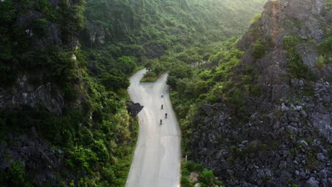 Following-a-group-of-motorcycles-winding-along-a-mountain-gorge-highway,-Ninh-Binh,-Vietnam,-aerial