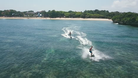Wave-jumping-on-Jetsurf-boards-in-a-clear-pristine-bay,-Bali,-aerial-follow-slow-motion