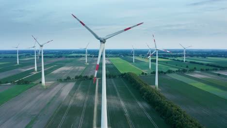 Aerial-drone-shot-of-windmills-in-industrial-renewable-energy-technology-park-with-tall-wind-turbines-spinning-in-green-dutch-farmland-drone-parallax-pan-view-4k