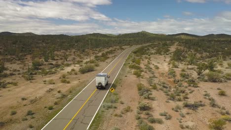 Gran-Autocaravana-Que-Aparece-En-La-Parte-Inferior-Izquierda-De-La-Toma-Conduciendo-Por-Las-Carreteras-Vacías-Del-Desierto-De-Baja-California