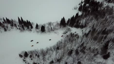 Drone-shot-from-above-of-snowmobile-riders-making-their-way-in-the-woods-in-Chibougamau,-Quebec