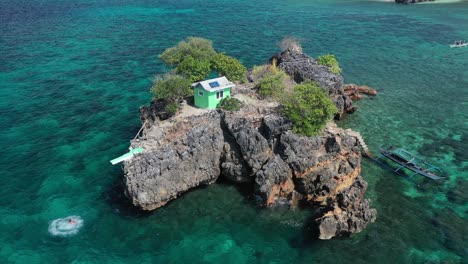 Static-Aerial-View-of-Man-Jumping-From-Platform-on-Rocky-Islet-Into-Turquoise-Sea,-Ramblon-Island-Archipelago,-Philippines