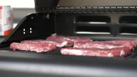 Raw-steaks-on-griddle-of-matt-black-outdoor-grill,-slow-motion