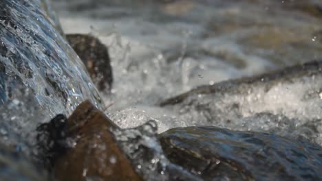 Close-up-of-crystal-clear-waterfall-splashing-onto-rocks-in-a-stream-slow-motion