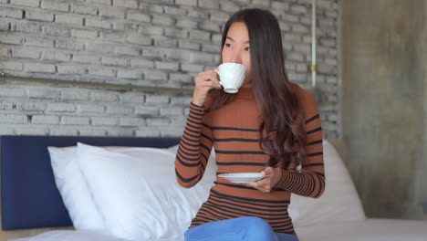 Junge-Asiatische-Frau,-Die-Morgens-Kaffee-Trinkt,-Lächelt,-Während-Sie-Auf-Einem-Betthotel-Sitzt