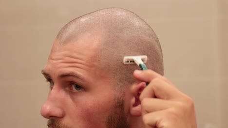 Close-up-of-young-man-shaving-his-own-bald-scalp-with-disposable-razor-inside-bathroom