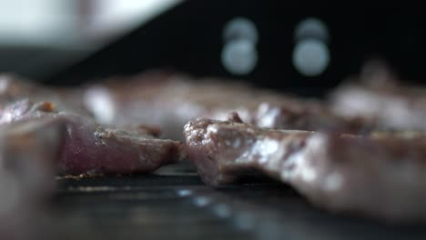Meat-being-grilled-on-a-grill-with-smoke,-close-up