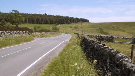 Vehicles-driving-past-on-a-small-highway-running-through-the-moorlands-of-Derbyshire,-England