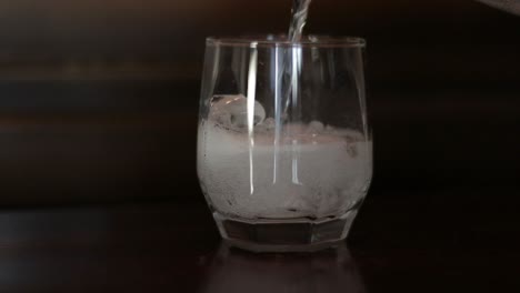 Pouring-soda-with-sparkling-bubbles-in-a-glass-with-ice-in-slow-motion