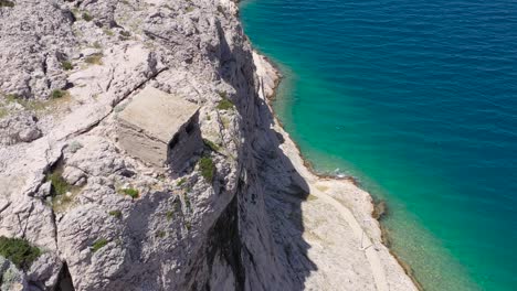 Sheep-enters-shelter-at-rock-cliff-in-Otok-Pag-island-Croatia-near-the-village-of-Metajna,-Aerial-flyover-view