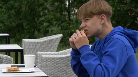 Young-man-sitting-in-outdoor-terrace-and-eating-sandwich-for-the-first-time-after-quarantine