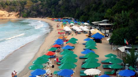 Beautiful-aerial-drone-dolly-shot-going-past-countless-colorful-tourist-umbrellas-with-people-enjoying-the-tropical-golden-sand-beach-at-the-famous-Praia-do-Madeiro-beach-near-Pipa-in-Northern-Brazil