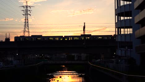 Silhouette-Eines-Japanischen-Zuges,-Der-An-Der-Brücke-über-Den-Fluss-Vorbeifährt,-Mit-Feurigem-Sonnenuntergang-Im-Hintergrund-In-Japan