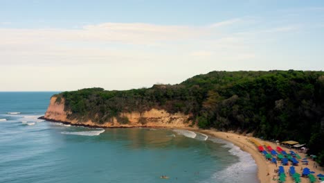 Wunderschöne,-Weit-Aufsteigende-Luftdrohnenaufnahme-Des-Tropischen-Strandes-Praia-Do-Madeiro-Mit-Farbenfrohen-Sonnenschirmen,-Die-Die-Küste-über-Den-Klippen-In-Der-Nähe-Der-Berühmten-Stadt-Pipa-Im-Norden-Brasiliens-Enthüllen