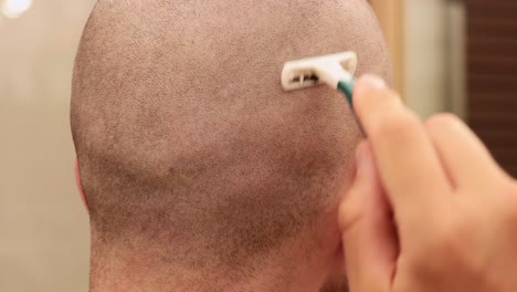 Close-up-view-of-a-young-man-shaving-the-back-of-his-own-bald-head-with-a-disposable-razor-blade