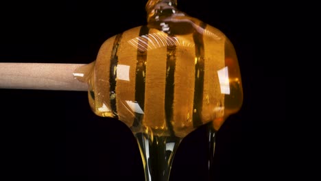 Macro-view-of-honey-dripping-over-honey-dipper-stick-with-black-background,-sexy-food-footage
