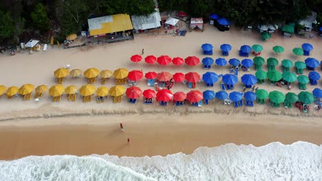 Gorgeous-aerial-drone-bird's-eye-top-view-flyby-of-the-tropical-beach-Praia-do-Madeiro-with-colorful-beach-umbrellas-and-tourists-swimming-and-surfing-near-the-famous-town-of-Pipa-in-Northern-Brazil