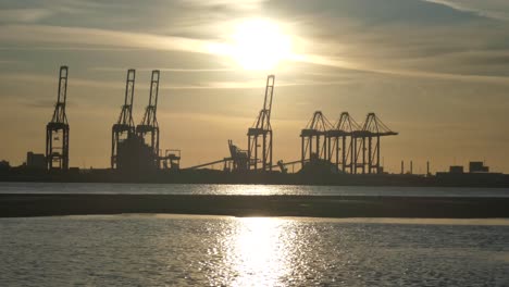 Silhouette-shipping-seaport-cargo-loading-cranes-on-shimmering-sunrise-water