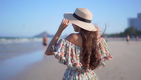 Back-view-of-a-woman-holding-a-hat-because-of-a-strong-wind-at-the-beach