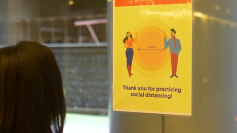 asian-woman-reads-social-distance-signage