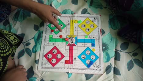 Asian-Indian-family-plays-Ludo-board-game-as-entertainment-on-covid19-lockdown,-man-rolls-the-dice,-top-down-view,-slow-motion-shot