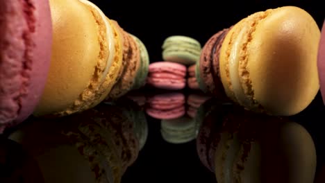 Macro-view-moving-past-macarons-on-black-reflective-glass,-sweet-tasty-desserts-interesting-low-down-perspective