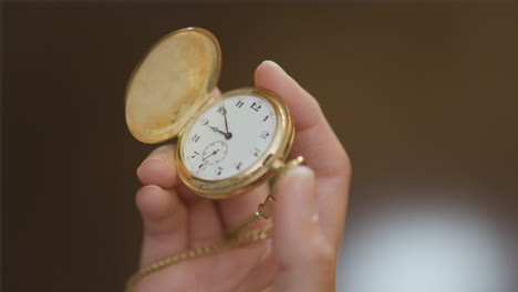 Woman's-hand-raises-a-pocket-watch-into-frame-and-opens-it-before-closing-it-back-up
