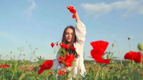 Kaukasische-Frau-Lässt-An-Einem-Sonnigen-Tag-Rote-Mohnblütenblätter-Von-Ihrer-Hand-Auf-Den-Boden-Im-Feld-Fallen,-Handheld-Aus-Der-Nähe