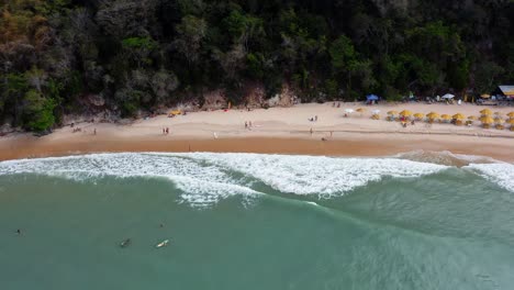 Gorgeous-aerial-drone-dolly-out-shot-of-the-tropical-beach-Praia-do-Madeiro-with-colorful-beach-umbrellas-and-tourists-swimming-and-surfing-near-the-famous-town-of-Pipa-in-Northern-Brazil