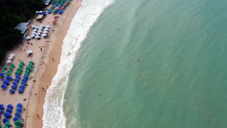 Gorgeous-aerial-drone-bird's-eye-top-view-of-the-tropical-beach-Praia-do-Madeiro-with-colorful-beach-umbrellas-and-tourists-swimming-and-surfing-near-the-famous-town-of-Pipa-in-Northern-Brazil