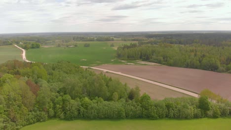 Drone-flying-over-countryside-landscape-in-Kurzeme,-Latvia,-cloudy-day