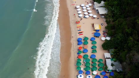 Hermosa-Vista-Aérea-De-Drones-Vista-Superior-Sobrevuelo-De-La-Playa-Tropical-Praia-Do-Madeiro-Con-Coloridas-Sombrillas-De-Playa-Y-Turistas-Nadando-Y-Surfeando-Cerca-De-La-Famosa-Ciudad-De-Pipa-En-El-Norte-De-Brasil