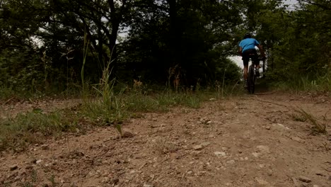Shot-from-below-of-a-cyclist-slowly-cycling-on-a-dirt-road-on-a-sunny-summer-day