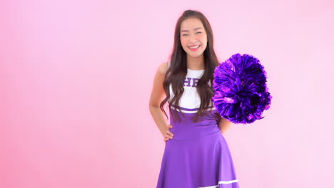 Hübsche-Asiatische-Cheerleaderin-Mit-Poms,-Die-In-Die-Kamera-Schauen-Und-Lächeln