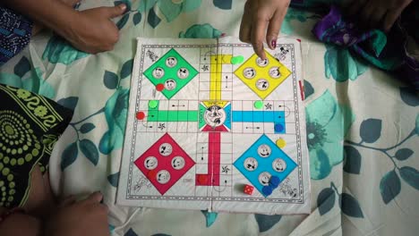 Asian-Indian-Family-playing-Ludo-board-game-on-bed-at-home,-female-hand-rolling-dice-top-down-view,-slow-motion