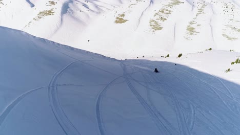 Scenic-view-of-fast-snowmobile-approaching-drone-on-white-snowy-mountain-with-snowmachine-track-lines-in-shadow-on-bright-sunny-day,-Akoura,-Lebanon,-backward-aerial
