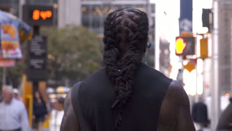 Afroamerican-black-man-with-long-dreadlocks-hair-walking-and-listening-to-music-in-slow-motion-in-New-York-City,-Manhattan,-with-the-radio-city-music-hall-in-the-background